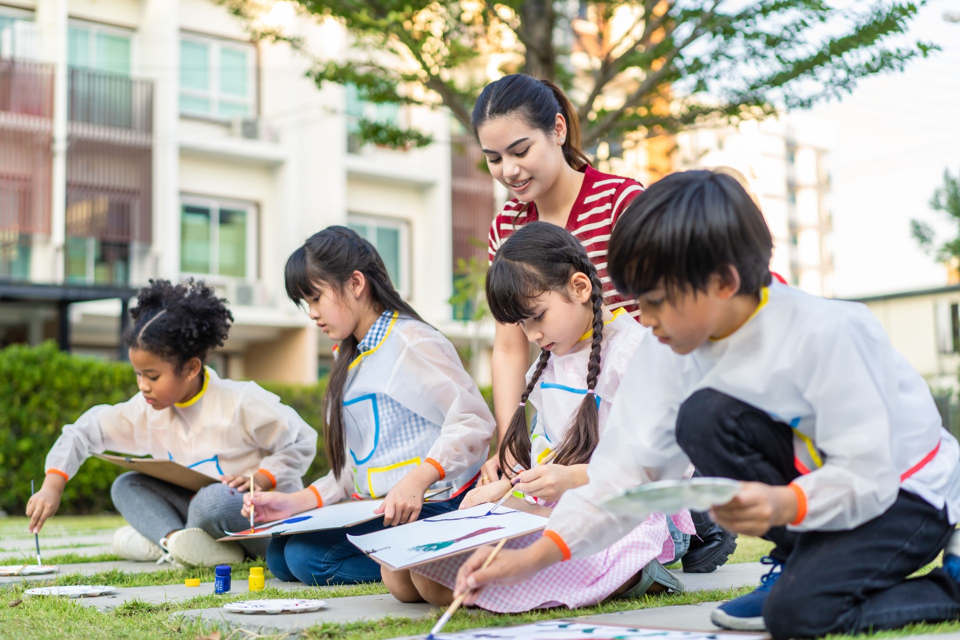 Group of student coloring on painting board outdoors in school garden. Adorable children learn how to draw art picture with watercolor paint and brush enjoy creative fun activity at elementary school.